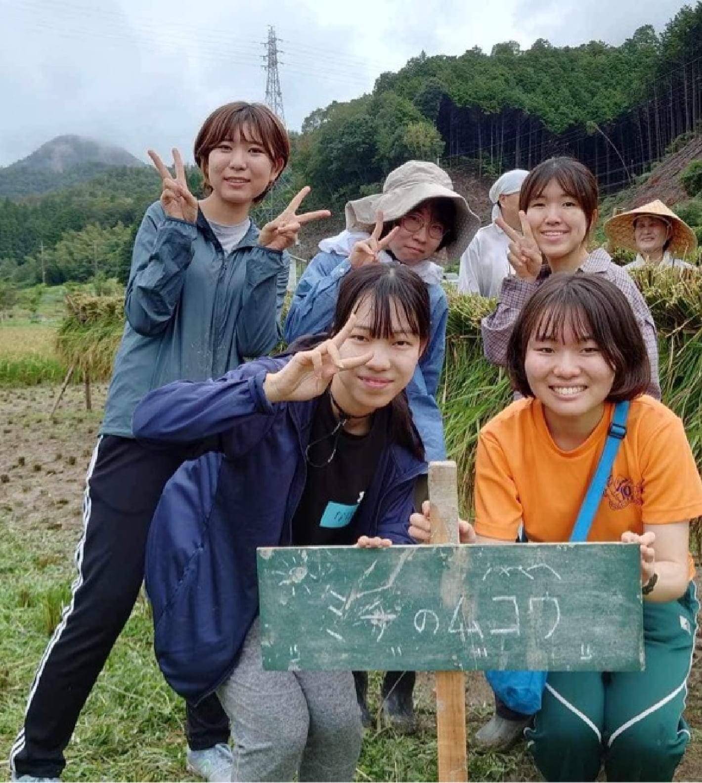 「ミチのムコウ」と書いてある看板を前に撮られた学生の集合写真